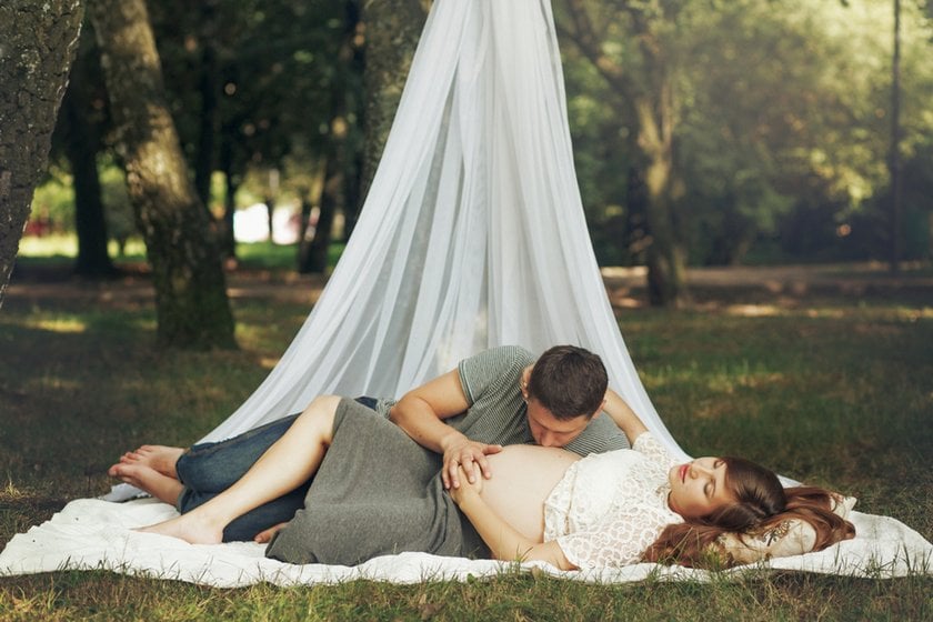 A man and his pregnant wife are sitting on a blanket in a park | Skylum Blog